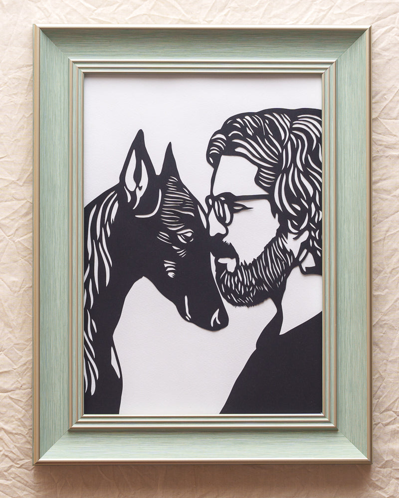 Detailed black paper-cut art depicting a Doberman Pinscher and its human companion, their heads touching gently in the center against a contrasting background.