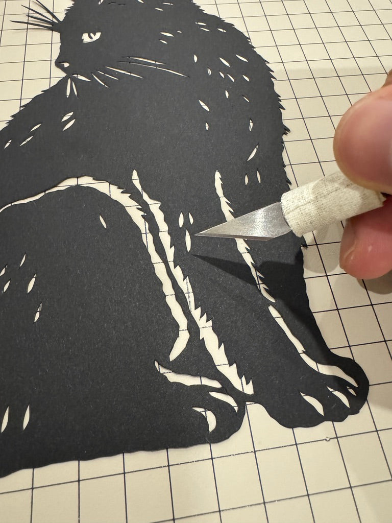 A hand holding a paper cut artwork of a pet, with visible scissors and cutout details—representing the traditional art of paper cutting used for pet memorials