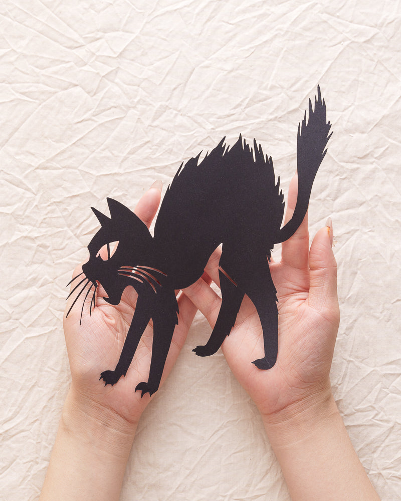 Hand-cut silhouette paper art of a cat shape, held on a person's palm