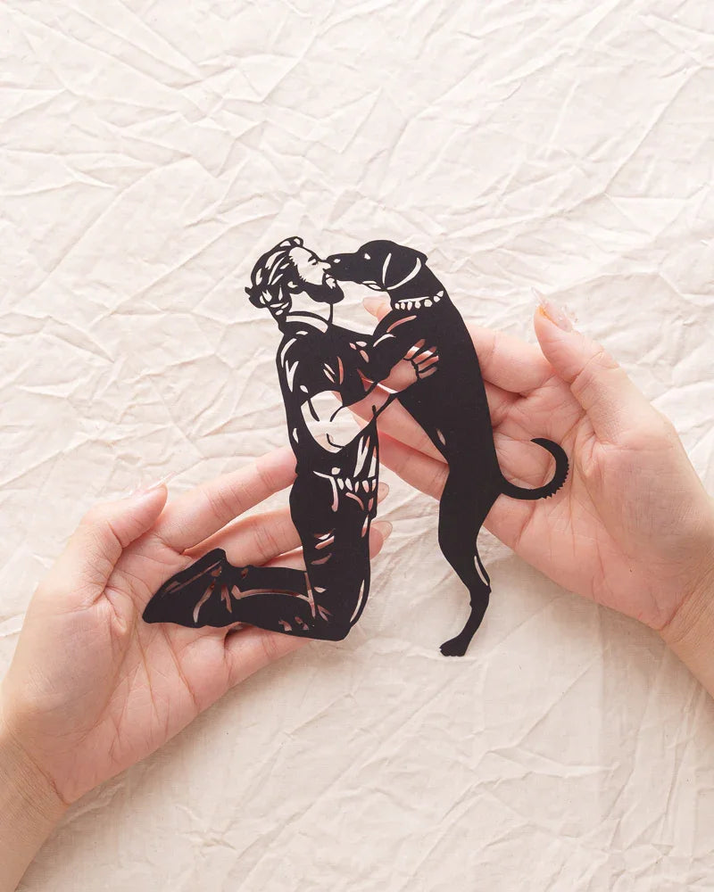 Holding a paper-cut artwork of a dog jumping up to kiss its owner — embodying the heartfelt bond between pets and humans