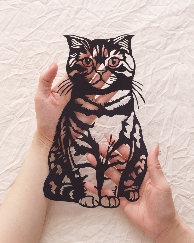 Cradling her paper twin: Silk-textured fur makes phantom purrs rumble under my fingertips 