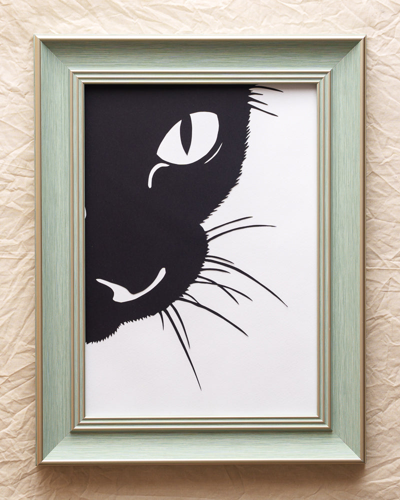 Hand-cut single-layer paper silhouette of a cat's head peeking curiously from the upper left corner