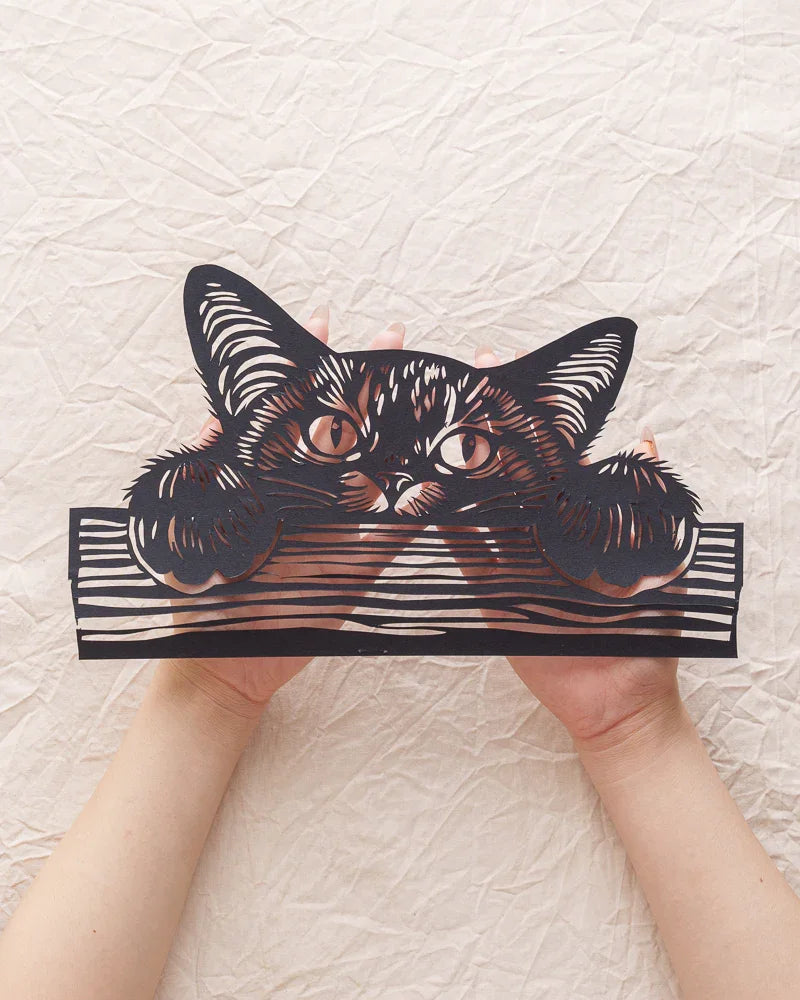 In my hands is a commemorative paper-cut artwork of a kitten peeking