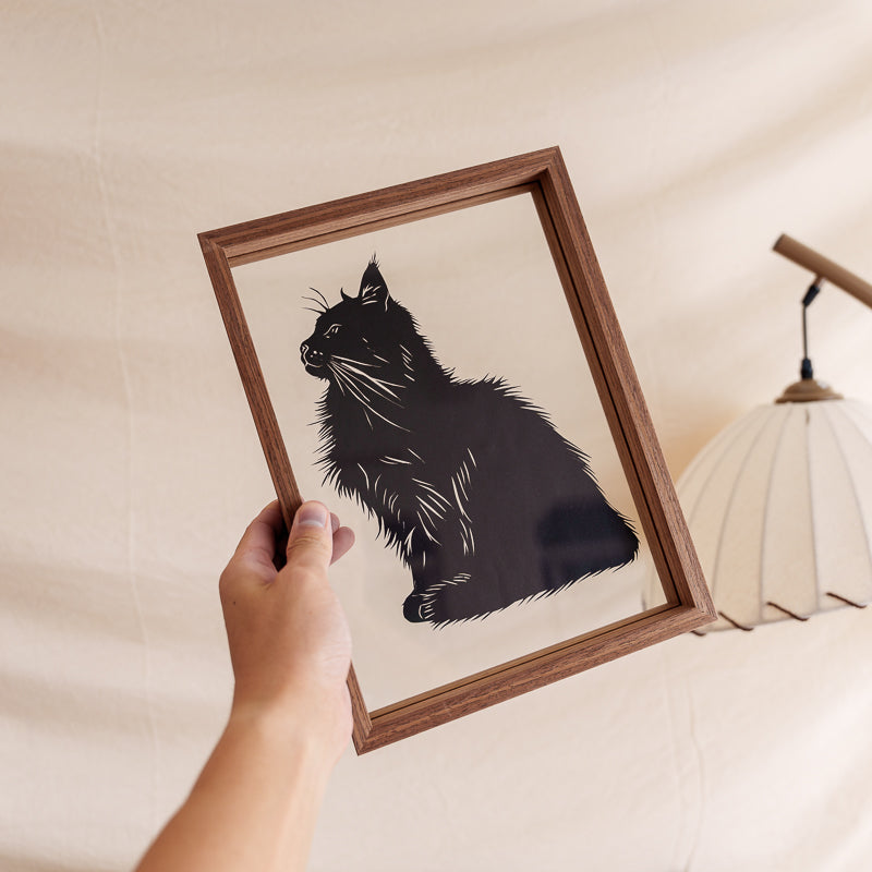 An artist holding a handmade framed cat papercut memorial, a personalized silhouette artwork created as a keepsake to cherish a pet’s memory.