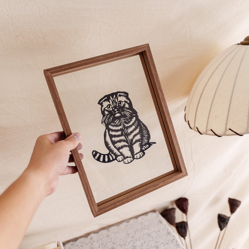 Artist holding a handmade framed cat silhouette papercut memorial, a personalized artwork designed to cherish the memory of a pet.