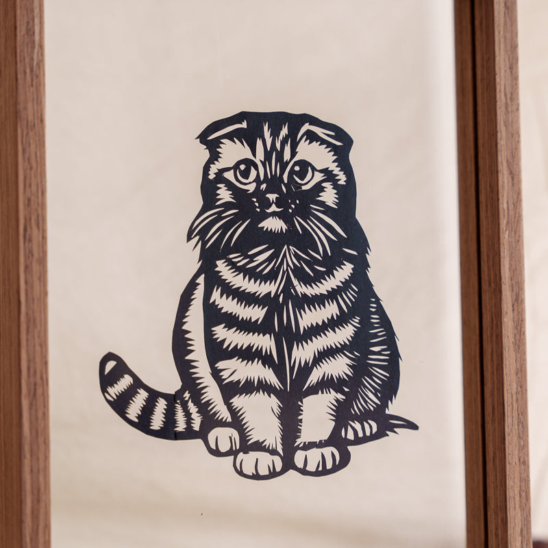 Close-up detail of handmade kitten papercut memorial, showing delicate carving techniques that capture the cat’s sad expression.