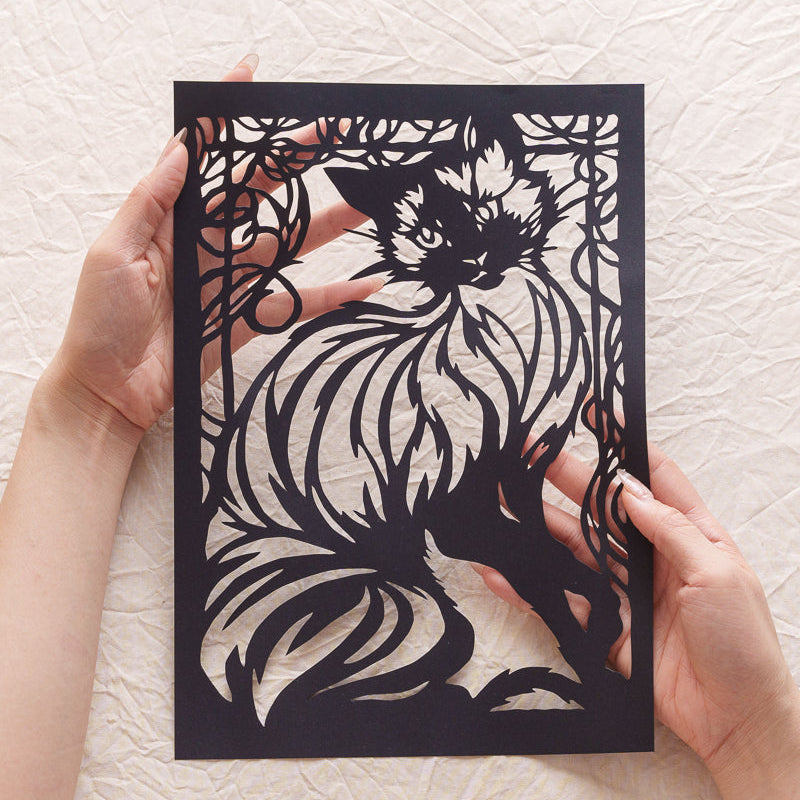A hand holding a delicately cut cat silhouette, designed as a custom tribute to a beloved pet.