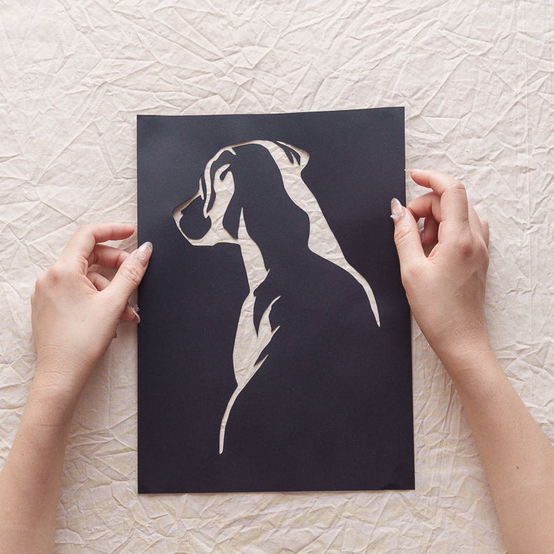 Hand holding a dog portrait silhouette memorial paper cut.
