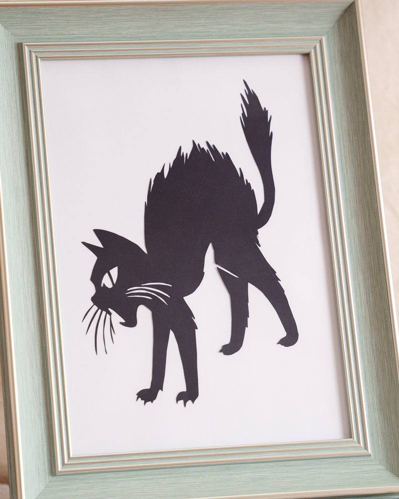 Silhouette-style hand-cut paper art capturing a cat's startled, arched-back pose