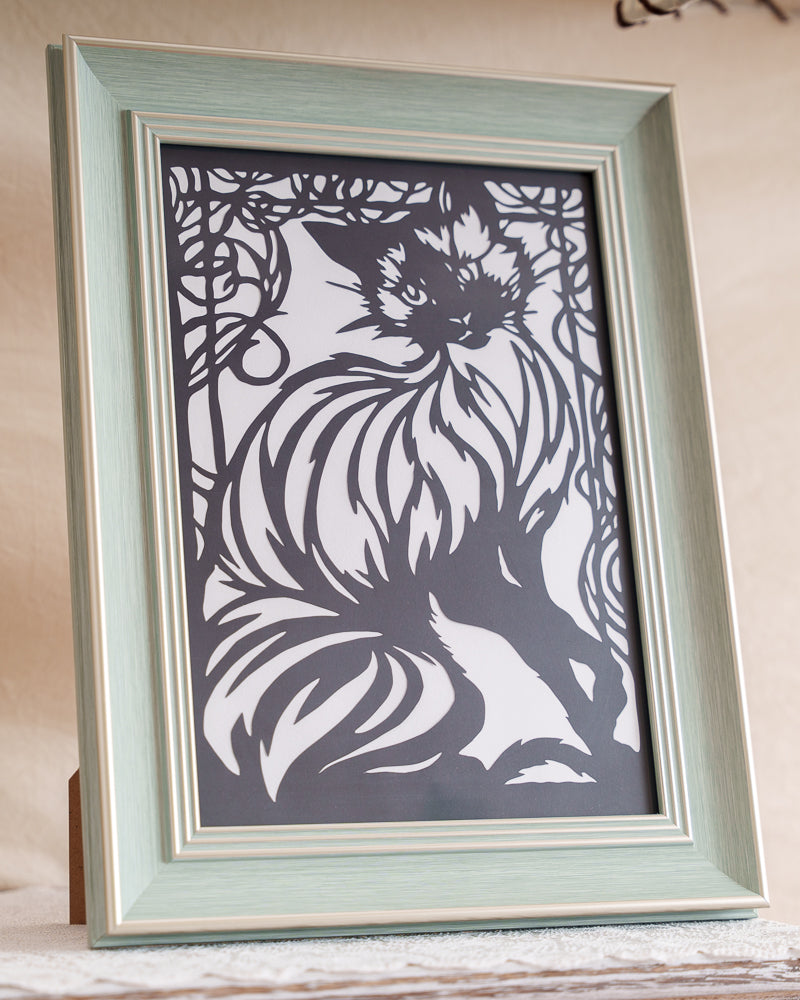 Hand-cut paper silhouette of a cat with flowing body lines and ornamental frame, expressing artistic remembrance.

