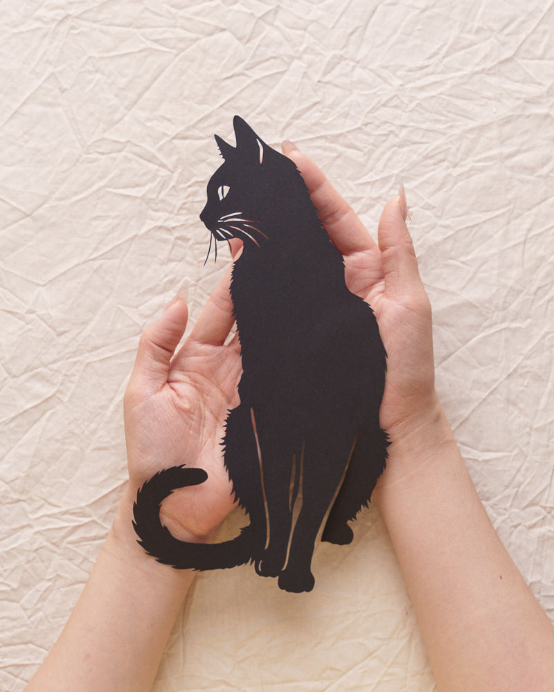 Person holding custom cat paper-cut art, highlighting hand-cut edges with backlit effect