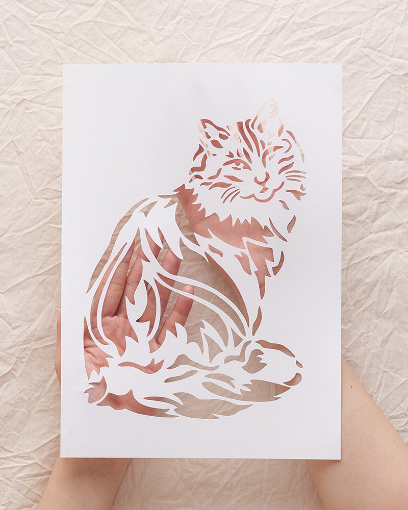 Close-up of a person's hand carefully holding an elegant white paper-cut portrait or silhouette of a Lionhead cat, showcasing its unique features.