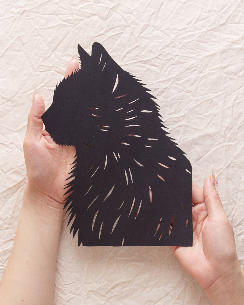 Close-up of a hand holding a delicate, hand-cut paper cat portrait