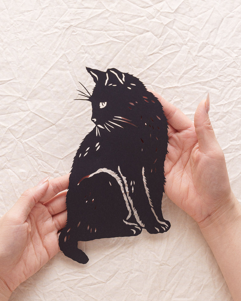 A hand holding a handmade paper cut silhouette in memory of a beloved cat.