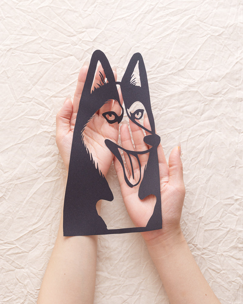Person holding carefully crafted husky papercut against solid background, fingers supporting edges