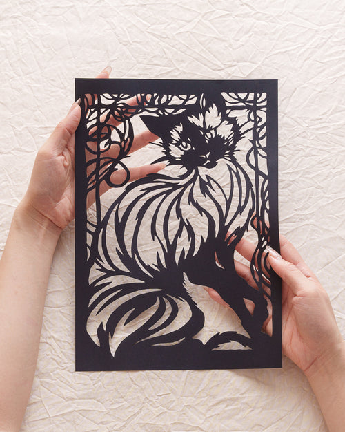 A hand holding a delicately cut cat silhouette, designed as a custom tribute to a beloved pet.