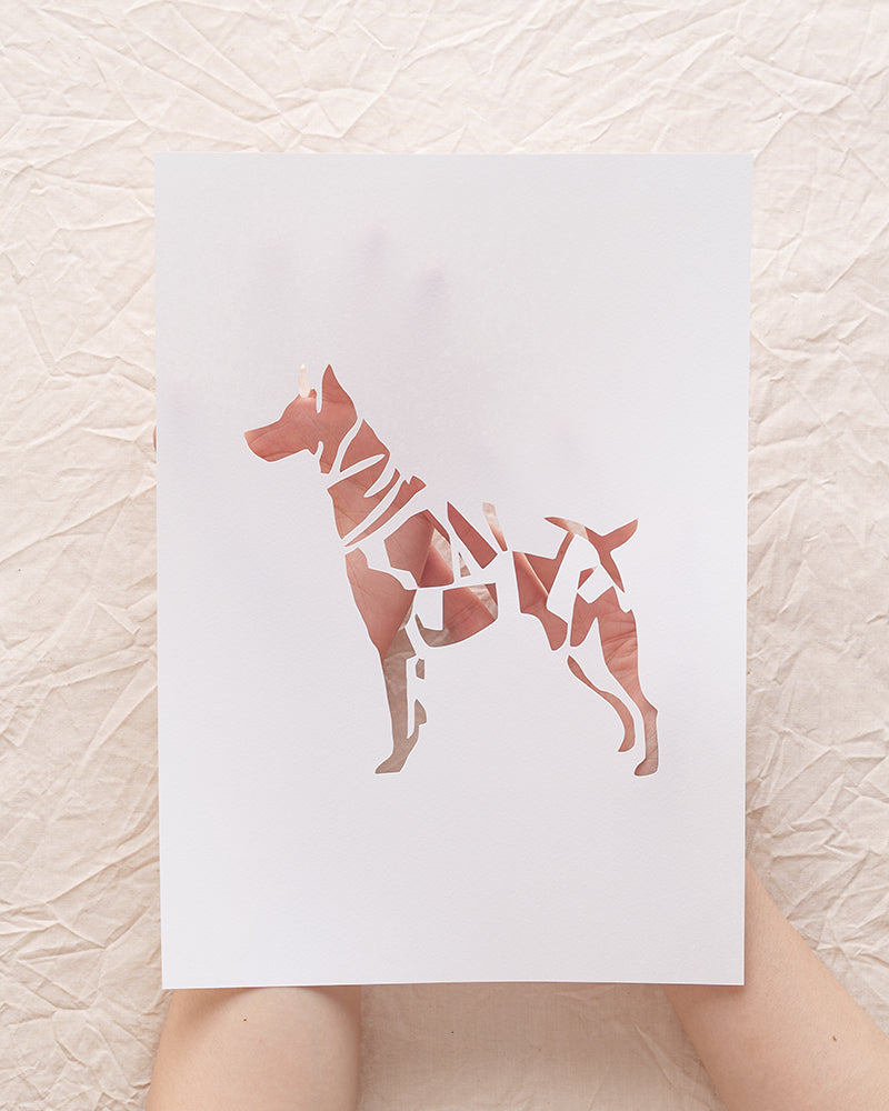 Close-up of a person holding a delicately crafted, custom paper-cut portrait of a dog