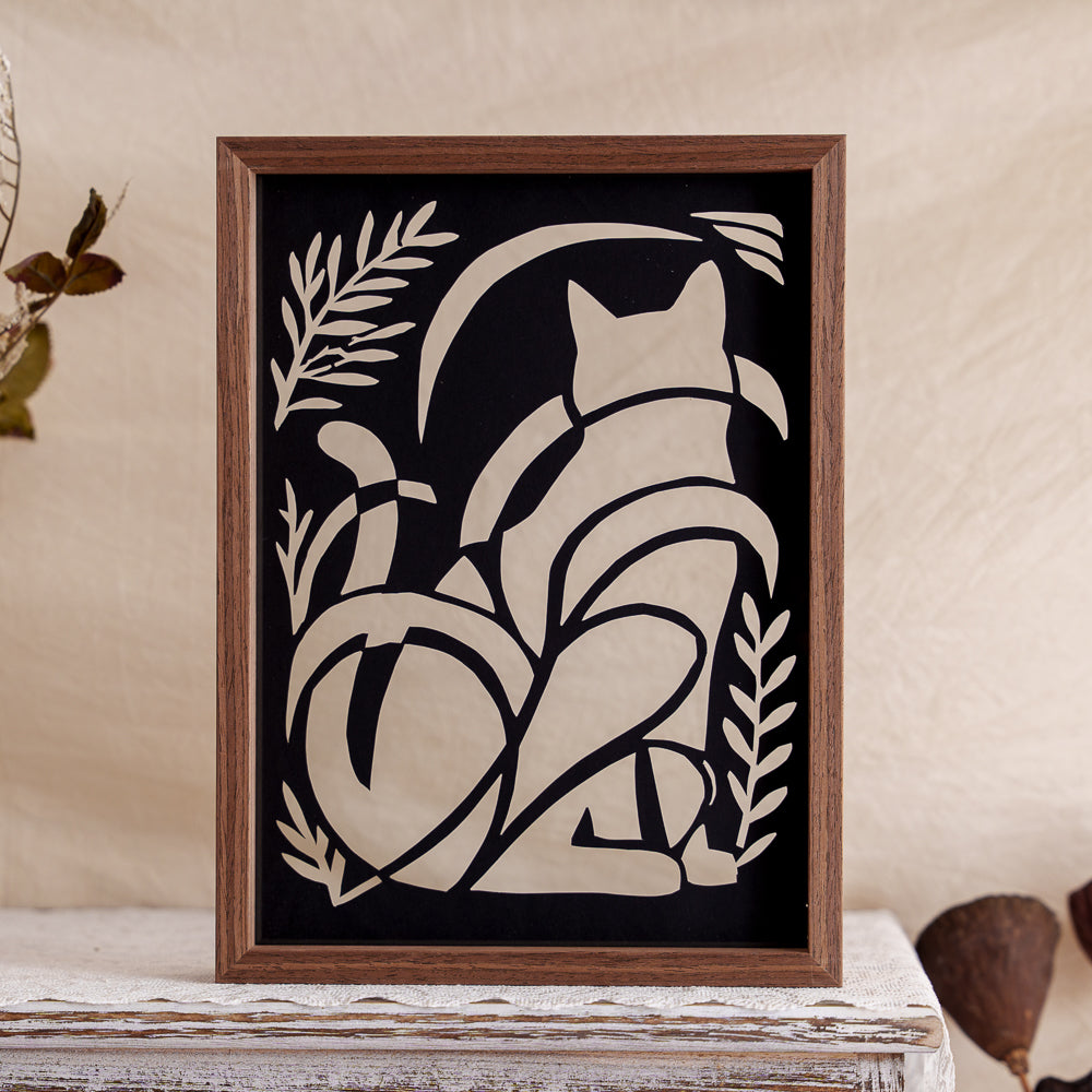 An artistic silhouette papercut featuring a cat in a garden setting, blending natural beauty with graceful feline form in a timeless design.