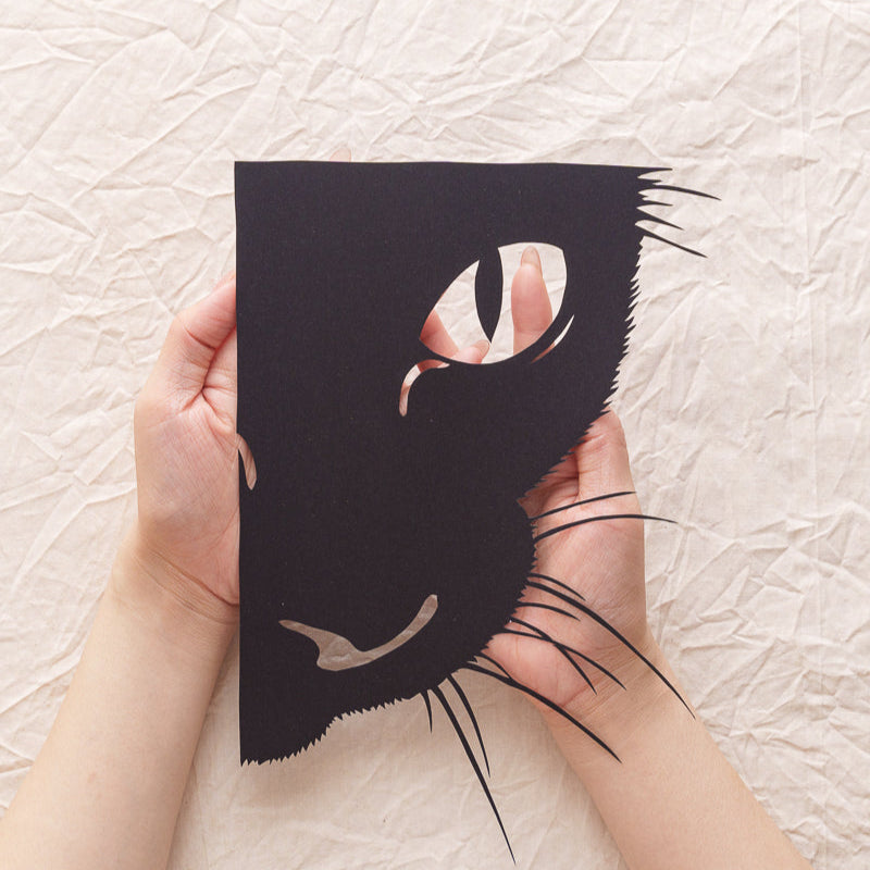Hand holding a handcrafted custom cat portrait paper cut memorial, with detailed fur and expressive eyes.