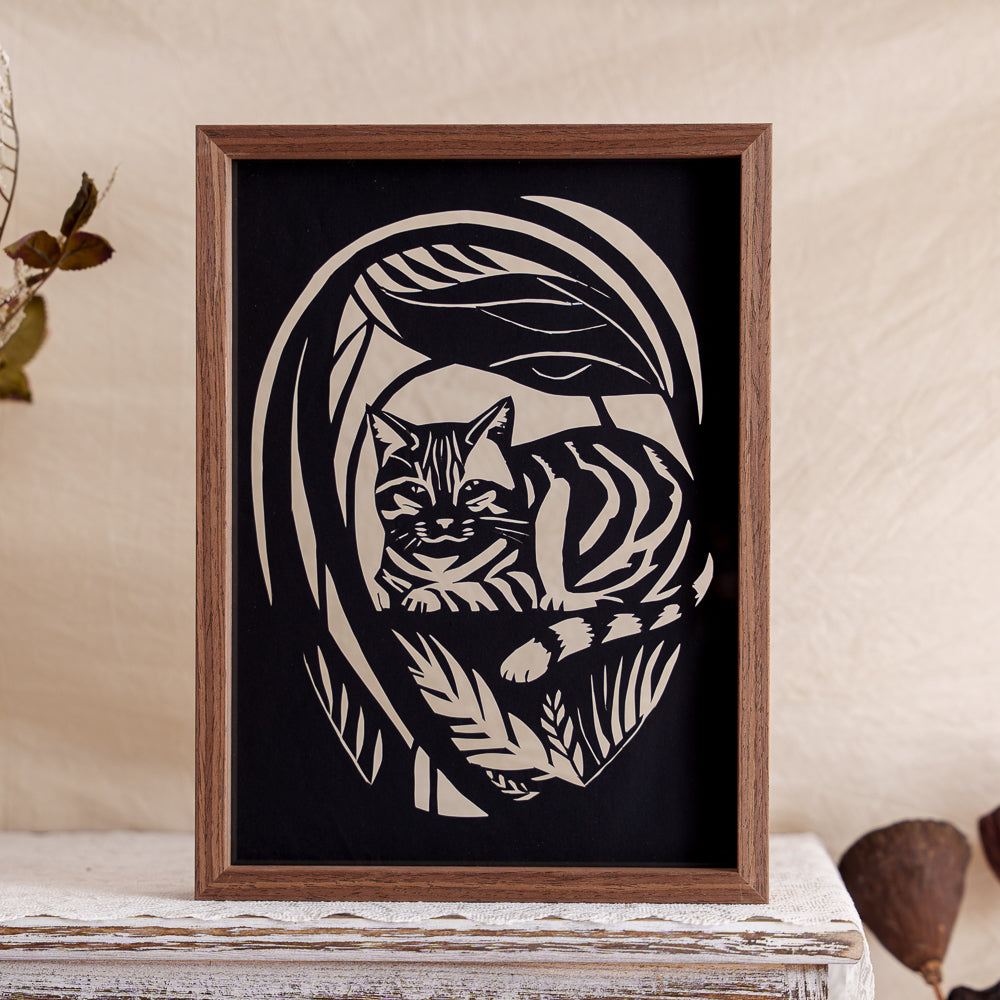 A peaceful memorial papercut artwork featuring a cat lying in a garden, surrounded by delicate floral details — a serene tribute to a cherished companion.