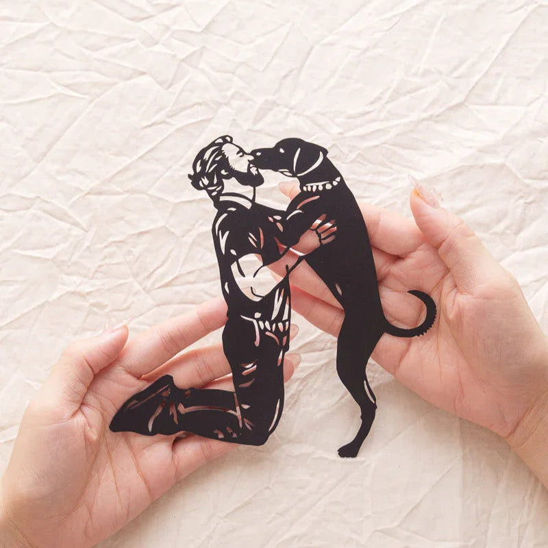 Holding a paper-cut artwork of a dog jumping up to kiss its owner — embodying the heartfelt bond between pets and humans