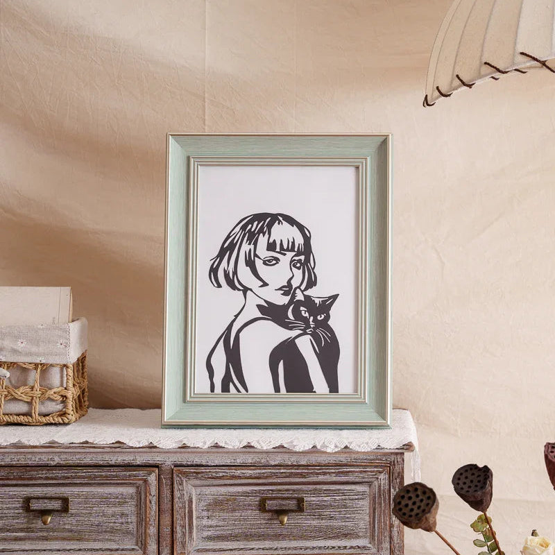 A framed papercut artwork of a woman holding her cat, beautifully displayed at home as a heartfelt tribute and decorative piece.