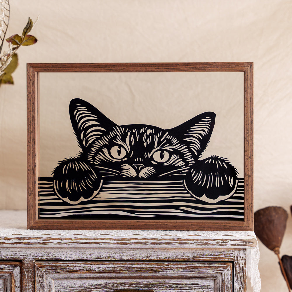 A memorial papercut capturing a curious kitten peeking over the edge of a table, paws resting on the surface — a playful moment frozen in time.