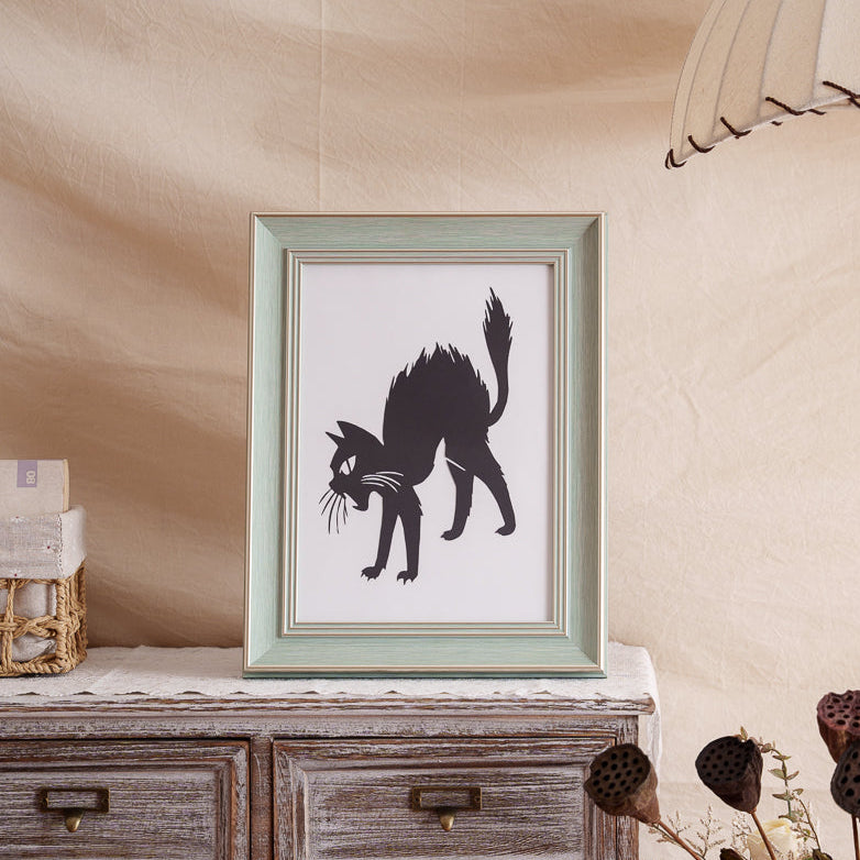 A framed cat paper cut memorial placed on a home shelf.