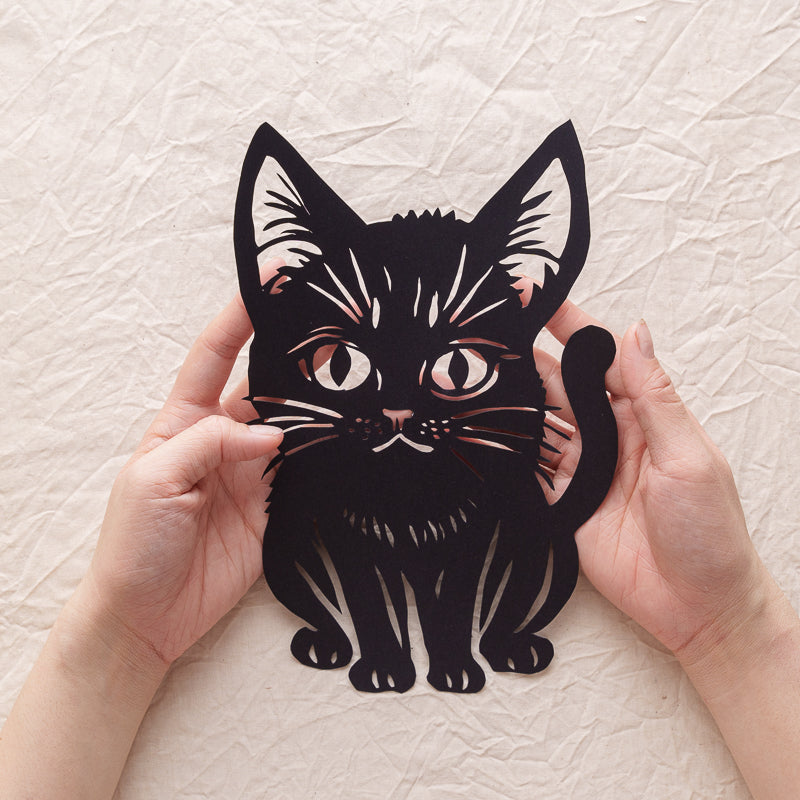 An artist holding a newly completed cartoon-style cat silhouette papercut.