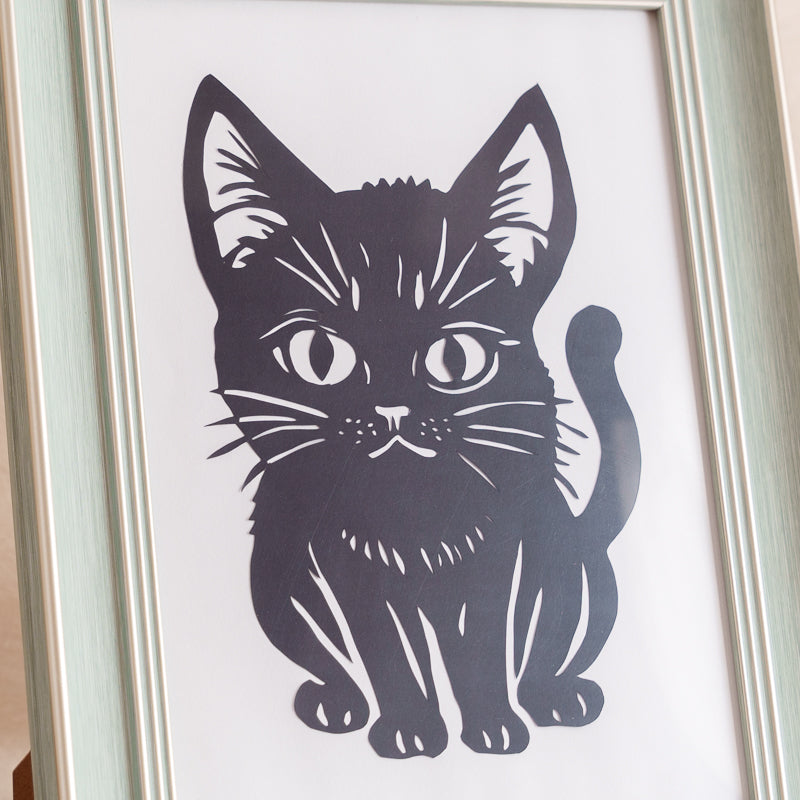 Close-up of a cartoon-style cat papercut showing fine hand-carved details.

