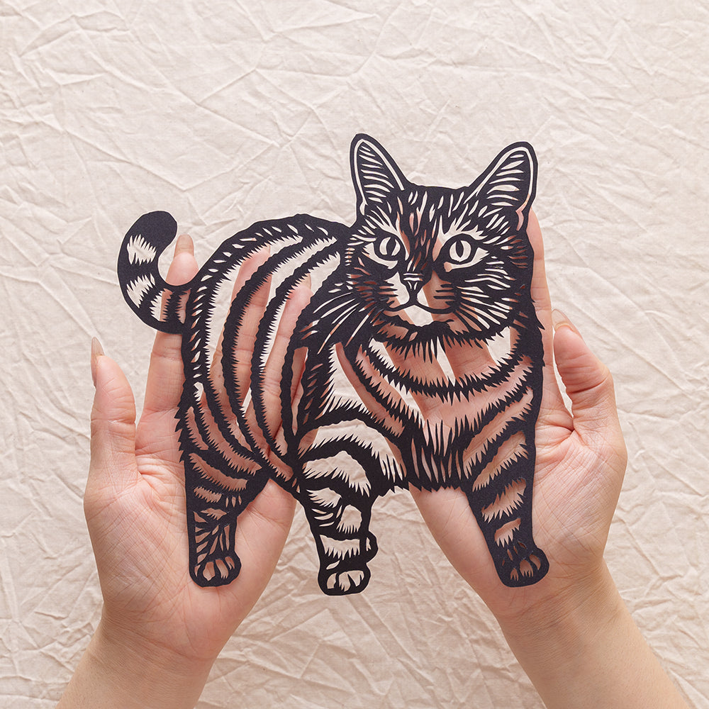 An artist holding a black cat memorial silhouette paper cut.