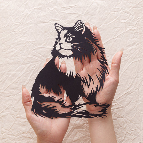 An artist holding a freshly completed handcrafted cat paper cut memorial.