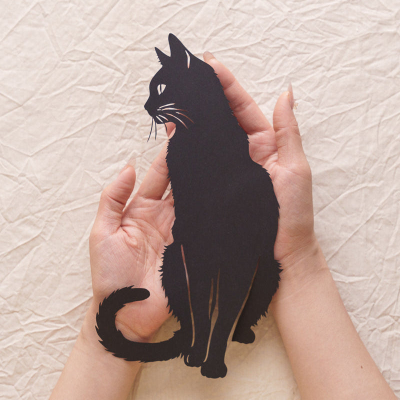 An artist holding a freshly carved cat silhouette paper cut artwork