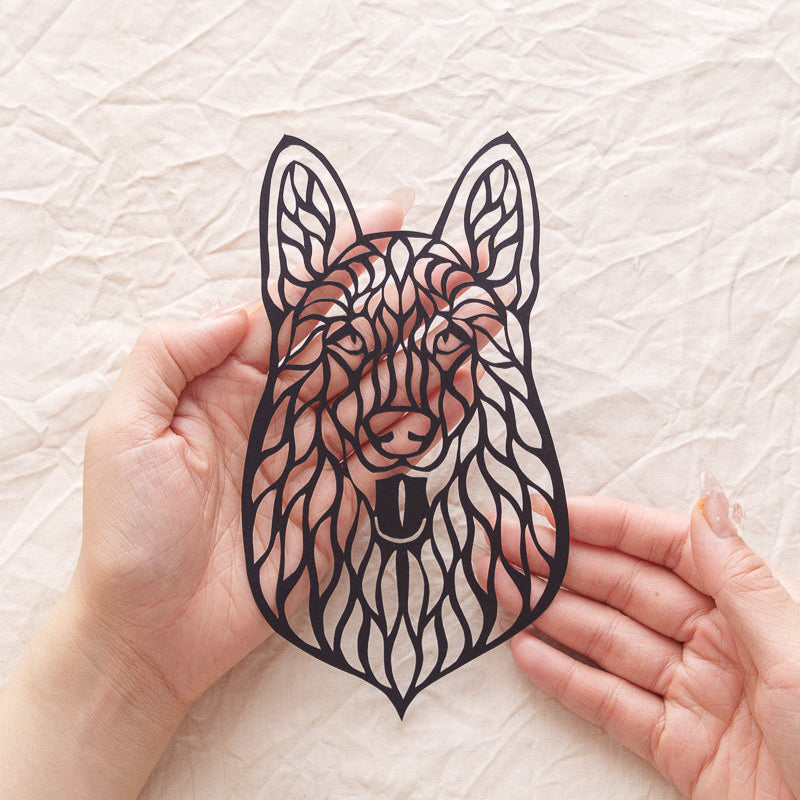 Close-up view of hands carefully holding an intricate, personalized hollow-cut paper silhouette portrait of a Husky