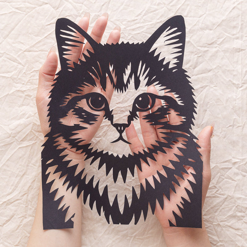 Close-up view of a person's hand gently holding a delicate, handmade silhouette portrait of a cat