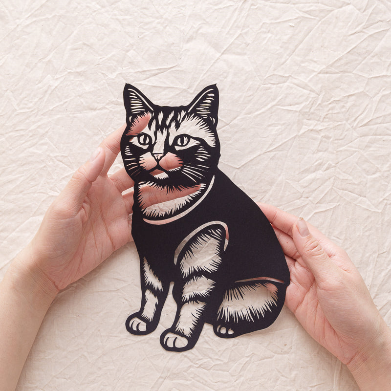 An artist holding a handmade cat memorial papercut, freshly completed.

