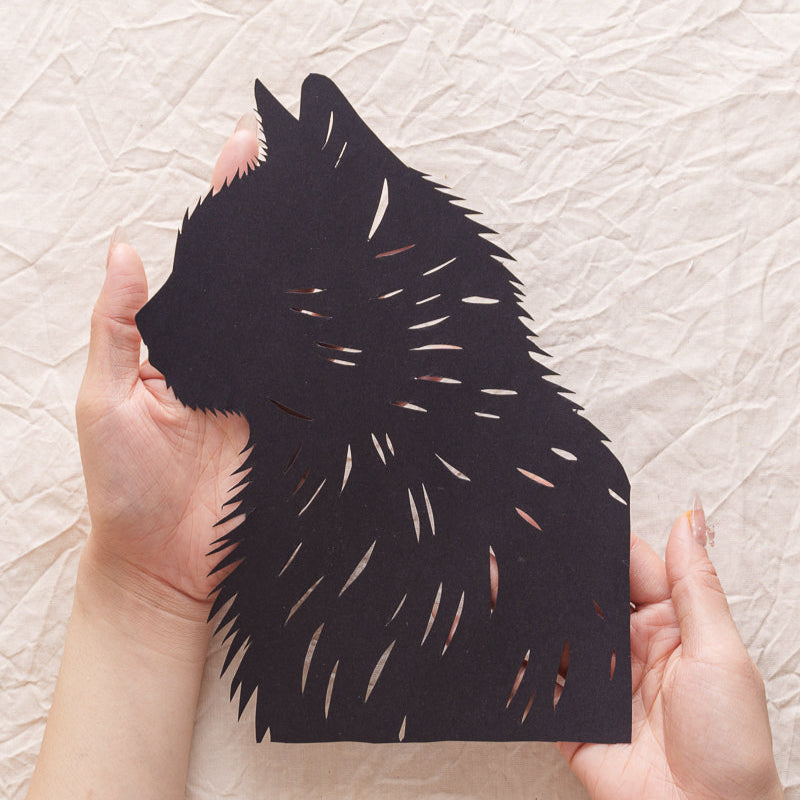Close-up of a hand holding a delicate, hand-cut paper cat portrait